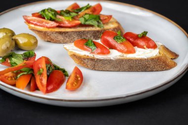 Siyah arkaplanda kiraz domatesli, peynirli, fesleğenli ve zeytinyağlı lezzetli bruschetalara yakından bakın. İtalyan mutfağı..