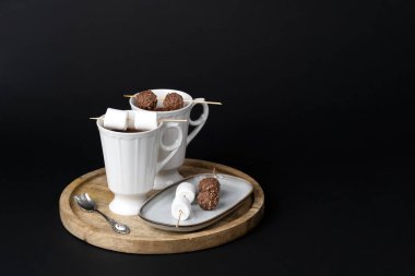 Two beautiful white porcelain cups of hot Chocolate drink with marshmallows and chocolates skewers over wooden table on black background. Winter time. Holiday concept.	