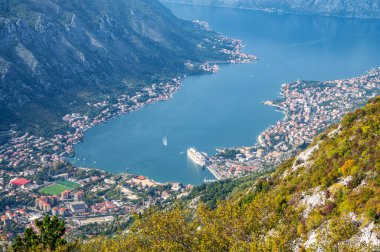 A panoramic aerial view of the Bay of Kotor, Monternegro with picturesque coastline, red roofs of houses and marina with boats and a large cruise ship.	