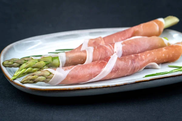 新鲜的芦笋 用深蓝色的盘子包裹在黑色的背景上 健康食品 顶部视图 — 图库照片