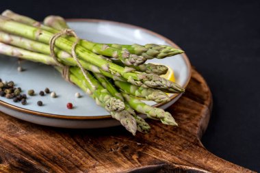 A bunch of fresh asparagus in a blue plate on a black background. Healthy food. 	