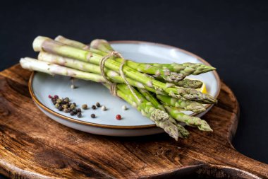 A bunch of fresh asparagus in a blue plate on a black background. Healthy food. 	
