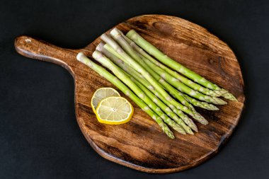 A bunch of fresh asparagus over a wooden board on a black background. Healthy food. 	