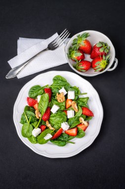 Çilekli taze yaz salatası, bebek ıspanağı, ceviz ve koyu arkaplanda beyaz peynir. Sağlıklı yiyeceklerin zarif sunumu.