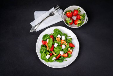 Çilekli taze yaz salatası, bebek ıspanağı, ceviz ve koyu arkaplanda beyaz peynir. Sağlıklı yiyeceklerin zarif sunumu.