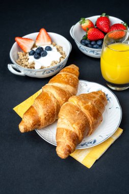 Meyveli sağlıklı kahvaltı, yoğurtlu yulaf ezmesi, portakal suyu ve koyu arkaplanda tereyağlı Fransız kruvasanı. Sağlıklı beslenme.
