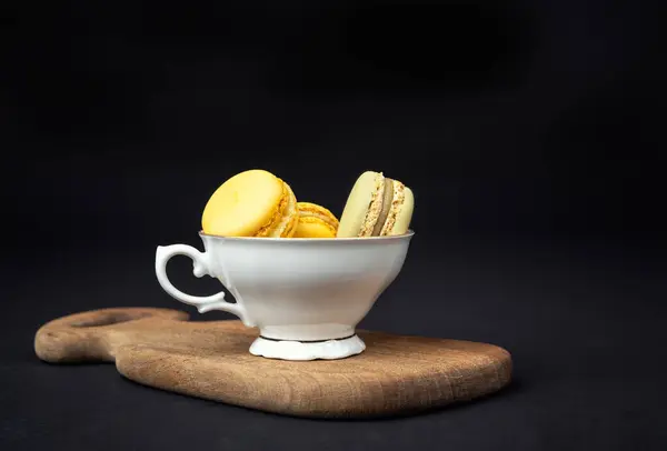 Still life with pistachios and orange macaroons arranged with beautiful fine porcelain in baroque style on a black background