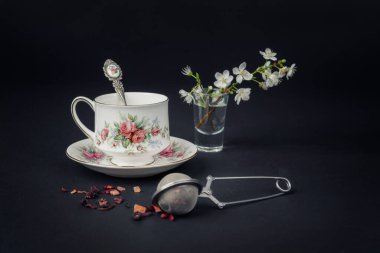 Güzel bir porselen çay fincanı ve siyah arka planda çay aksesuarları ile sakin bir hayat.