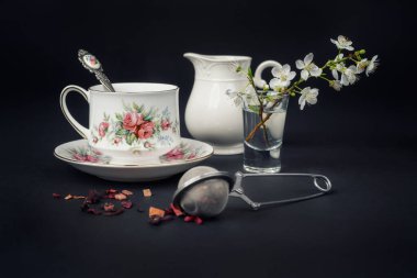 Güzel bir porselen çay fincanı ve siyah arka planda çay aksesuarları ile sakin bir hayat.