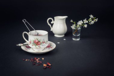 Güzel bir porselen çay fincanı ve siyah arka planda çay aksesuarları ile sakin bir hayat.