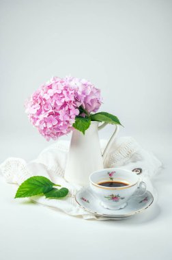 Vazoda çiçek açan pembe bir ortanca buketi ve beyaz arka planda porselen bir fincan kahveyle hayat.