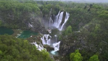 Hırvatistan 'ın yeşil bir bahar ormanındaki göllü ve pitoresk şelaleli Plitvice Ulusal Parkı' nın inanılmaz bir klibi. Büyük Şelale 'nin etrafında İHA uçuşu.