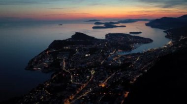 Eski kasaba Dubrovnik 'in muhteşem panoramik klibi, aydınlatılmış caddeler, binalar ve gün batımında tekneleri olan marina..