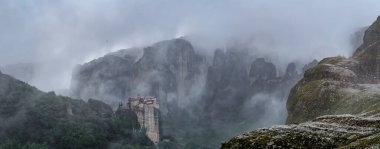 Amazing panoramic view of the cliffs in the Meteora valley and the monasteries mysteriously shrouded in mist and low clouds near Kastraki, Greece. clipart