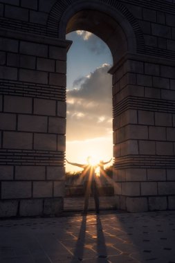Silhouette of a woman sending the last rays of the sun at sunset, standing under the arch of an ancient building, part of the ruins of the Great Basilica near Pliska, Bulgaria.	