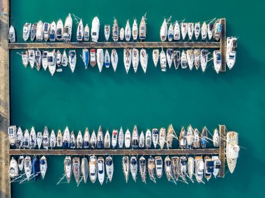 Slovenya 'nın Izola kentindeki marinada sıra sıra park etmiş yat ve teknelerin panoramik hava manzarası. Çapalı teknelerle üst görünüm.