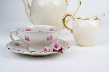 Güzel bir porselen çay fincanı, çay aksesuarları ve beyaz arka planda zarif bir porselen çaydanlıkta pembe çiçek açan bir dalla hayat.