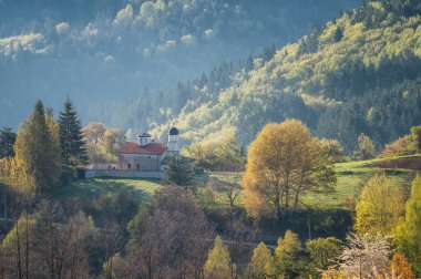 A spring mountain valley in a sunny morning with an old small chapel among rich vegetation and spruce dark dense forests near Smolyan, Rhodopi Mountains, Bulgaria.	