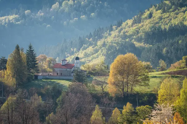 A spring mountain valley in a sunny morning with an old small chapel among rich vegetation and spruce dark dense forests near Smolyan, Rhodopi Mountains, Bulgaria.	
