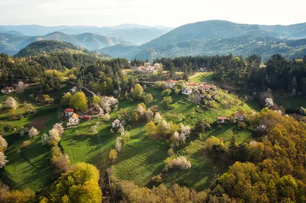 Zengin bitki örtüsü, çiçek açan ağaçlar ve çevrelerinde küçük evler bulunan bahar tepeleri, Bulgaristan 'ın Rodop Dağları, Smolyan kasabası civarındaki sabah ışığında yıkandı..
