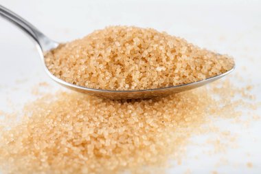 Beyaz arka planda gümüş kaşıkta kahverengi şeker