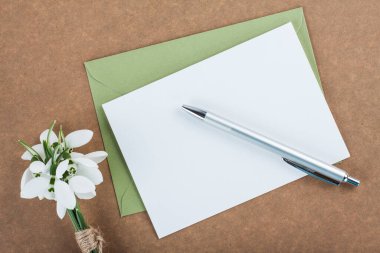 Tahta arka planda bir davetiye kartı, içinde kartopu çiçekleri ve bir kalem var.