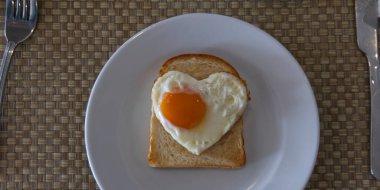 Kalp şeklinde yumurta ve kızarmış çavdar ekmeği beyaz seramik tabakta. Sevgililer Günü konsepti. Kahvaltı tasarımına bayılırım. Şenlikli öğle yemeği ya da kahvaltı.