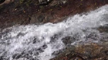 Şelaleden akan hızlı su akıntısı güneş ışığı altındaki kayalıklara doğru akıyor. Temiz su arka planı. Yüksek kalite 4k görüntü