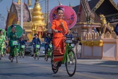 Chiang Mai, Thailand - January 20, 2023: Pretty women holding beautiful umbrellas in traditional costumes and riding cycling bicycles annual show at San Kamphaeng, Bosang umbrella festival.