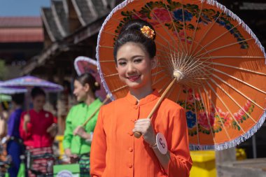 Chiang Mai, Thailand - January 20, 2023: Pretty women holding beautiful umbrellas in traditional costumes smiled at the participants of the annual event show San Kamphaeng, Bo sang umbrella festival.