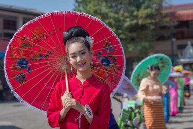 Chiang Mai, Thailand - January 20, 2023: Pretty women holding beautiful umbrellas in traditional costumes smiled at the participants of the annual event show San Kamphaeng, Bo sang umbrella festival.