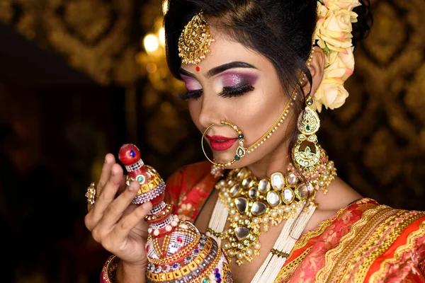Magnificent young Indian bride in luxurious bridal costume with makeup and heavy jewellery holding traditional wooden sindur or sindoor box in hand. Wedding Fashion and Lifestyle.