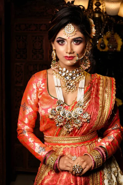 Magnificent young Indian bride in luxurious bridal costume with makeup and heavy jewellery with classic vintage interior in studio lighting. Wedding Fashion and Lifestyle.