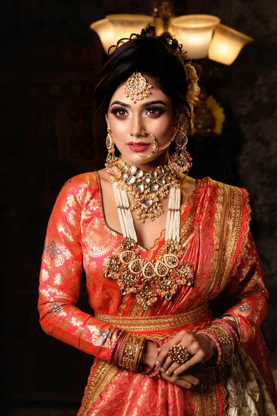 Magnificent young Indian bride in luxurious bridal costume with makeup and heavy jewellery with classic vintage interior in studio lighting. Wedding Fashion and Lifestyle.