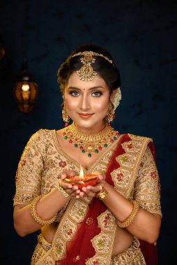 Geleneksel lehenga giymiş güzel bir Hintli kadının portresi, altın mücevherler ve bilezikler dekoratif arka planda el ele tutuşmuş. Hint kültürü, olay, din ve moda.