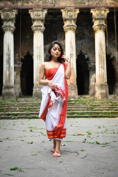 stock image Portrait of beautiful Bengali woman in red and white traditional ethnic saree and jewellery in front of a heritage building in Kolkata, India on March 16, 2023. Indian culture, religion and fashion.