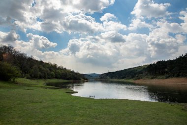 Mavi gökyüzü ve bulutlu, güneşli bir bahar günü. Küçük bir hedef ve çimenli bir manzara. Nehrin güzel manzarası. Arka plan bulutlu. Doğa