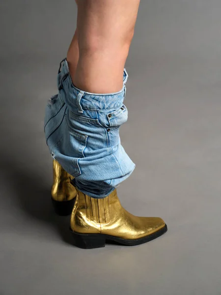 Close up view of woman wearing high heel shoes. Blue jeans isolated on grey background. Wearing gold leaf shoes, the woman had her jeans down. When the white girl is about to put on or take off her blue jean pants. Fashion and casual style