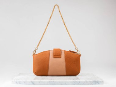 Şatafatlı kadınların çantası. Beyaz arka planda, mermer zeminde lüks turuncu ve bej renkli deri çanta. Altın zincirli bir çanta. Kadınlar için şık aksesuarlar. arka taraf