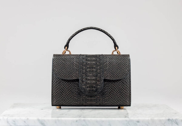 Luxury women 's bag. Luxury black leather handbag on white background, on marble floor. Crocodile skin look in black tones