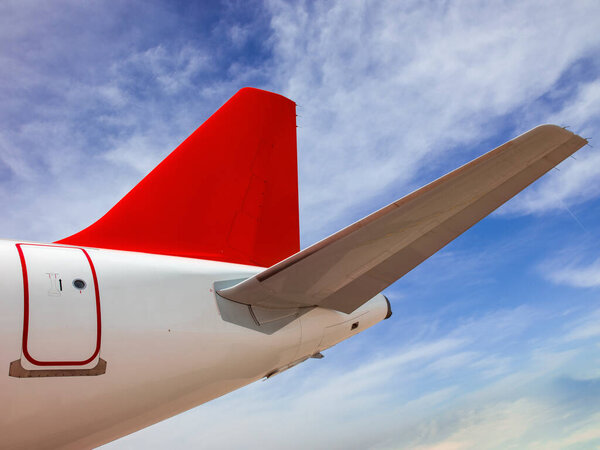 Airplane on blue sky background. Underside view of the aft, tail side of the passenger aircraft. State-of-the-art jet airliner with a red tail and a blue sky and clouds behind it