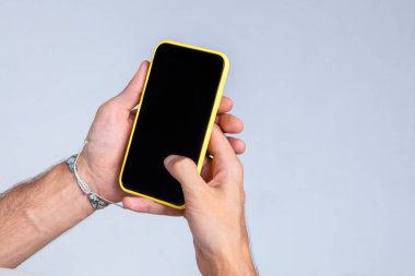 Beyaz bir arka planda, iki eliyle akıllı telefonu tutan bir erkek. Stüdyoda yakın çekim fotoğrafçılık. Telefon ekranı boş, reklam veya resim yerleştirmek için uygun.