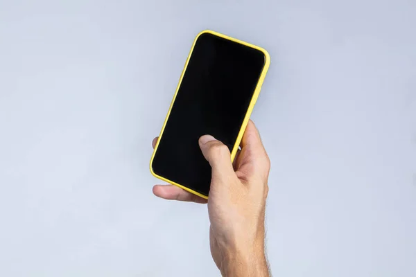 Sağ eliyle akıllı telefonu tutan ve baş parmağıyla ekranda çalışan bir adamın eli. Telefon ekranı boş ve siyah, reklam ya da resim koymak için uygun. Beyaz arkaplan