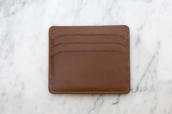 Brown wallet with brown leather wallet on white marble table
