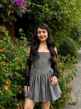 Kameraya çeşitli pozlarda poz veren tatlı bir kız. Çiçeklerin ve yeşilliklerin önünde güzel, esmer bir kız..