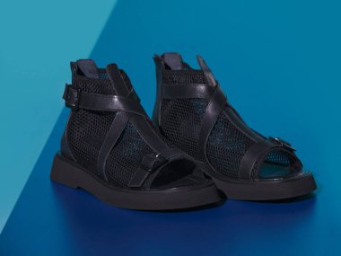 El örgüsü ve deri kumaştan yapılmış yaz sandaletleri. Özel tasarlanmış, kışlık botlara benzeyen yaz ayakkabıları, dekoratif bir stüdyoda çekilmiş. Mavi ve turkuaz arkaplan