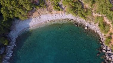 Drone kamerası denizin üzerinde uçarken harika görüntüler çeker. Turkuaz Akdeniz üzerinde uçarken küçük bir körfeze giriyoruz. Harika bir manzara ve güzel bir çekim. Dağlar ve deniz iç içe geçmiş.