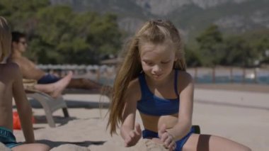 Genç bir aile, anne, baba ve iki çocuk sahilde eğleniyor. Bir kız ve bir oğlanla mutlu bir aile. Çocuklar kumda oynuyor, ebeveynler dinlenme odasında dinleniyor. Yaz tatlısı konsepti