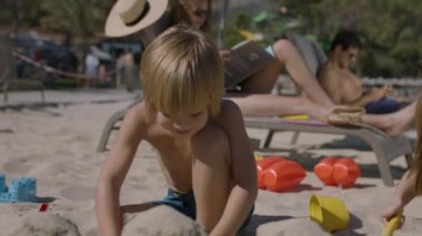 Genç bir aile, anne, baba ve iki çocuk sahilde eğleniyor. Bir kız ve bir oğlanla mutlu bir aile. Çocuklar kumda oynuyor, ebeveynler dinlenme odasında dinleniyor. Yaz tatlısı konsepti