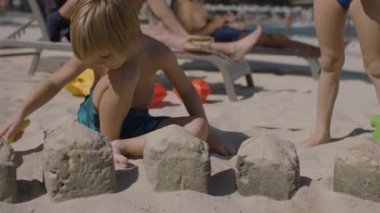 Genç bir aile, anne, baba ve iki çocuk sahilde eğleniyor. Bir kız ve bir oğlanla mutlu bir aile. Çocuklar kumda oynuyor, ebeveynler dinlenme odasında dinleniyor. Yaz tatlısı konsepti